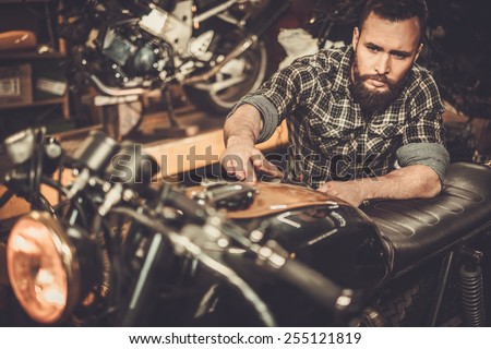 Mechanic building vintage style cafe-racer motorcycle in custom garage Mechanic building vintage style cafe-racer motorcycle in custom garage