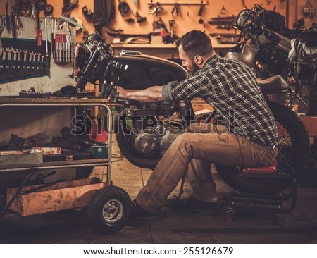 Mechanic building vintage style cafe-racer motorcycle in custom garage Mechanic building vintage style cafe-racer motorcycle in custom garage