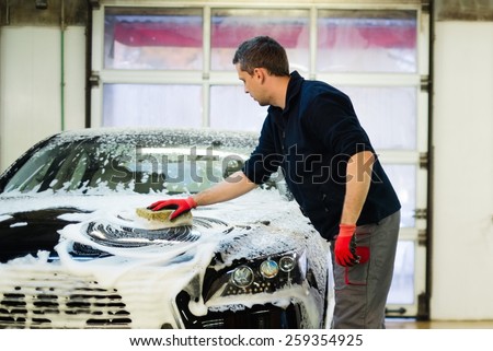 Man worker washing luxury car with sponge on a car wash