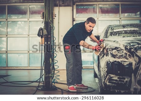 Man worker washing luxury car with sponge on a car wash