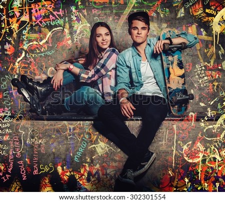 Young couple with skateboard outdoors against graffiti painted wall