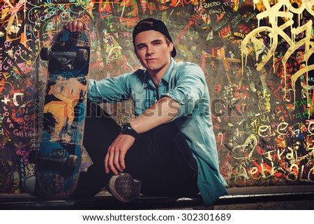 Handsome young man with skateboard outdoors against graffiti painted wall