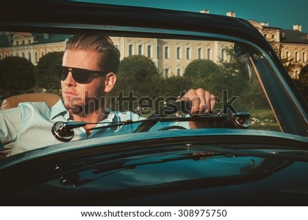 Confident wealthy young man behind classic convertible steering wheel