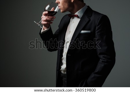 Sharp dressed man wearing jacket and bow tie with glass of vine