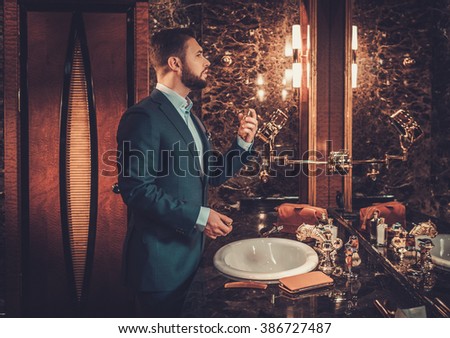 Confident well-dressed man using perfume in luxury bathroom interior.