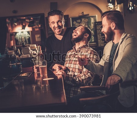 Cheerful old friends having fun and drinking draft beer at bar counter in pub.