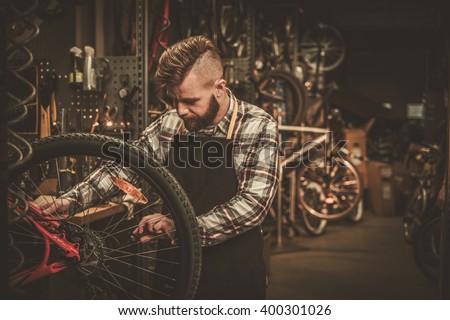 Stylish bicycle mechanic doing his professional work in workshop.