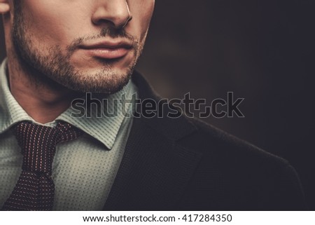 Serious well-dressed hispanic man posing on dark background.