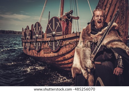 Viking warrior with sword and shield standing near Drakkar on the seashore.