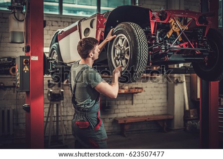 Mechanic working on classic car wheels and suspension in restoration workshop