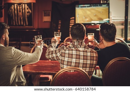 Cheerful old friends watching sports and drinking draft beer in pub.