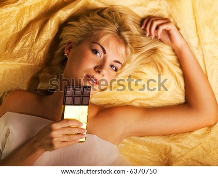 Beautiful girl with a chocolate craving lying on luxury golden fabric