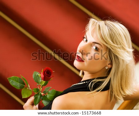 Beautiful young woman standing on a red carpet and holding a rose