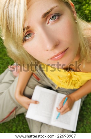 Sad young girl sitting outdoors on a grass and reading book