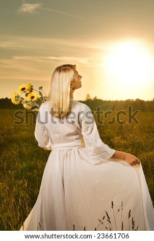 Young beautiful woman with a bouquet of sunflowers in the field at sunset