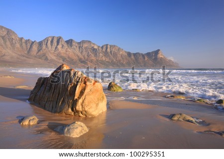 Rocky beach with coastal mountains, blue sky and sand near Cape town, South Africa.