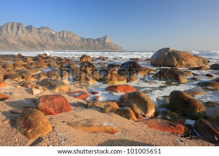 Coastal landscape with rocky beach and distant mountains near Cape Town, South Africa.