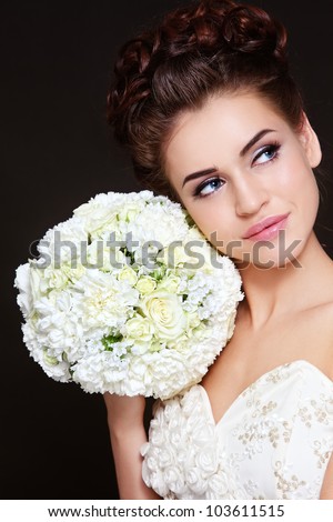 Portrait of young beautiful bride with stylish make-up and hairdo holding bouquet in her hand
