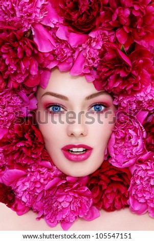 Portrait of young beautiful excited blue-eyed woman with pink peonies around her face