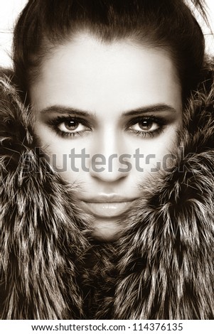 Close-up sepia portrait of young beautiful woman with stylish make-up and fur around her face