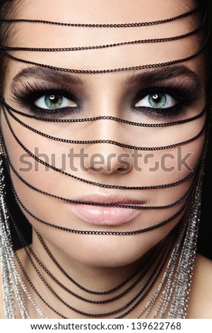 Close-Up Portrait Of Young Beautiful Green-Eyed Woman With Fancy Make-Up And Chains Over Her Face