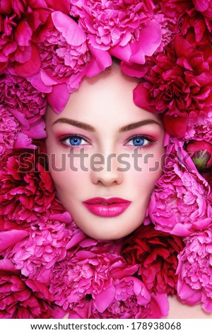 Portrait of young beautiful blue-eyed woman with pink peonies around her face