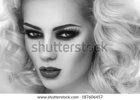 Black and white close-up portrait of young beautiful woman with smoky eyes and blond curly hair