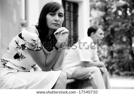 Black and white shot of young sad woman and man sitting on marble steps in park, selective focus