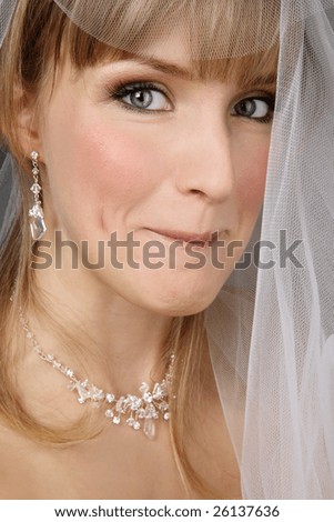 Portrait of beautiful bride looking from under bridal veil with sly smile
