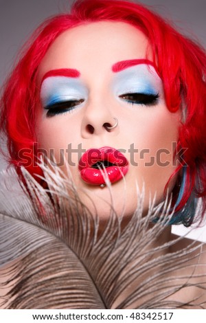 Close-up portrait of redhead woman with fancy make-up blowing on feather, selective focus