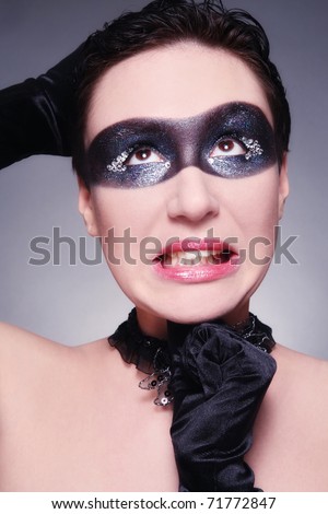 Humorous portrait of young woman with fancy mask painted on her face and confused expression