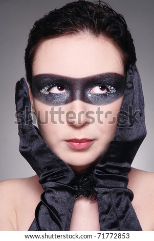 Humorous portrait of young woman with fancy mask painted on her face and thoughtful expression