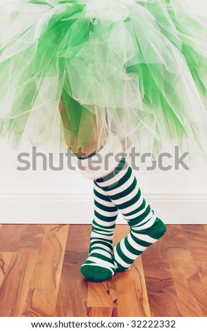 A young girl wearing a green and white tutu and socks