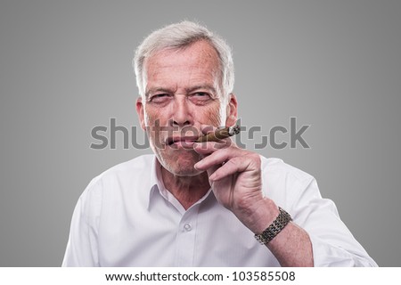 Handsome senior smoking a cigar. Handsome senior man with a shrewd expression and strong personaity smoking a cigar isolated on a grey studio background