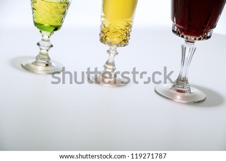 Low angle crop on white background of three cut glass wine glasses, filled with a selection of white and red wines