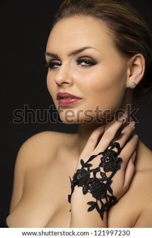 Closeup head and shoulders studio portrait of an exotic beauty with sultry eyes and bare shoulders posing with her hand in a black lace glove raised to her neck
