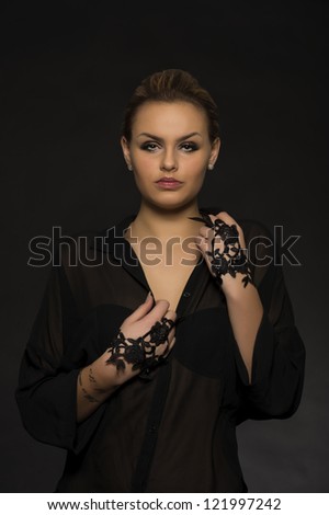 Dark studio portrait of a beautiful elegant woman in evening attire standing looking at the camera with a serious expression