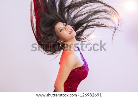 Beautiful woman in a stylish red gown tossing her long straight brunette hair high in the air