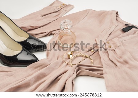 Elegant ladies fashion ensemble with a stylish dress, classic patent leather black court shoes, gold bangles and bottle of perfume or scent laid out ready to wear on a white background, low angle