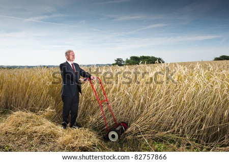 Businessman in Wheat Field. Man in a dark business suit cutting down wheat in a farm field. Metaphor for harvesting the fruits of your labor