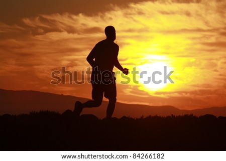 A silhouette of a man running on a trail with with the sun ricing up in the morning