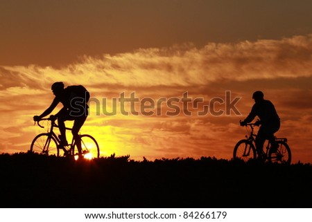 a silhouette of two people riding there bikes on a trail  in the early morning sun rise