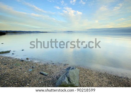 calm water in the Bay with blue sky\'s and clouds reflecting off the water rock on the shore
