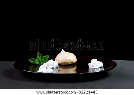 A Meringue Cookie on a Black Plate with a mint sprig and Whipped Cream
