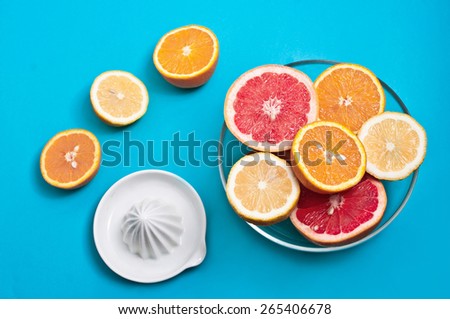 Oranges lemons and pink grapefruits in a bowl and a squeezer on a blue background