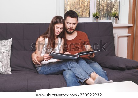 Young couple Leafs family album at home.Beautiful couple sitting on sofa at home and flips through the album.