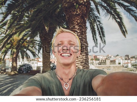 Young tanned guy shoots self-portrait in a background of palm trees