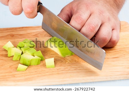 Chef cuts peeled avocado on a cutting board closeup