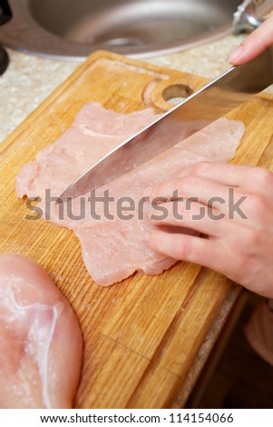Hand with knife cutting chicken meat