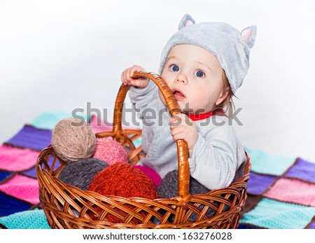 Little baby sitting in basket with balls of wool